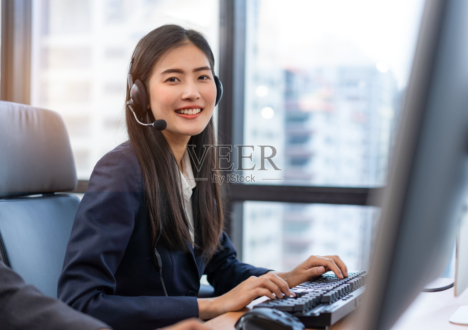快乐微笑的接线员亚洲女性客户服务代理戴着耳机在呼叫中心的电脑上工作，用她的服务思想与客户交谈，帮助解决问题照片摄影图片