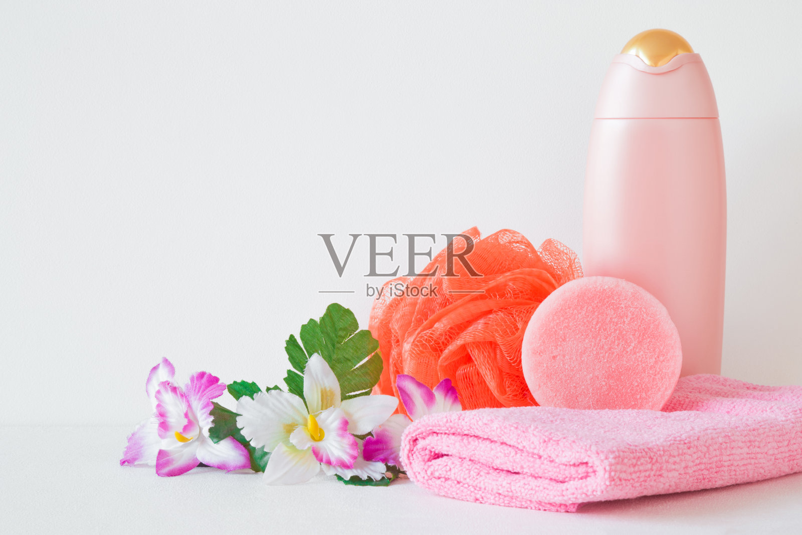 粉色的洗发水瓶，肥皂，毛巾和橙色的一缕。五彩缤纷的鲜花。简单的女性沐浴产品。特写镜头。前视图。灰色背景上的文本或标识的空白位置照片摄影图片