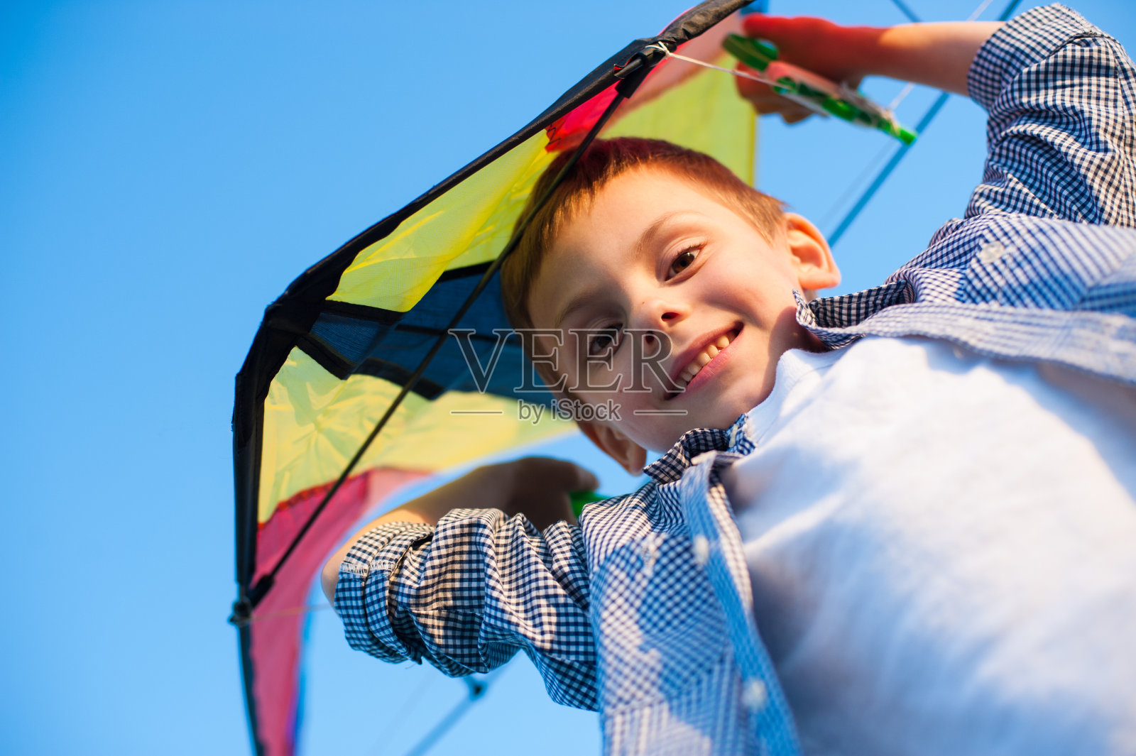 快乐微笑的小男孩与玩具风筝头顶在蓝天背景在夏天阳光明媚的一天照片摄影图片