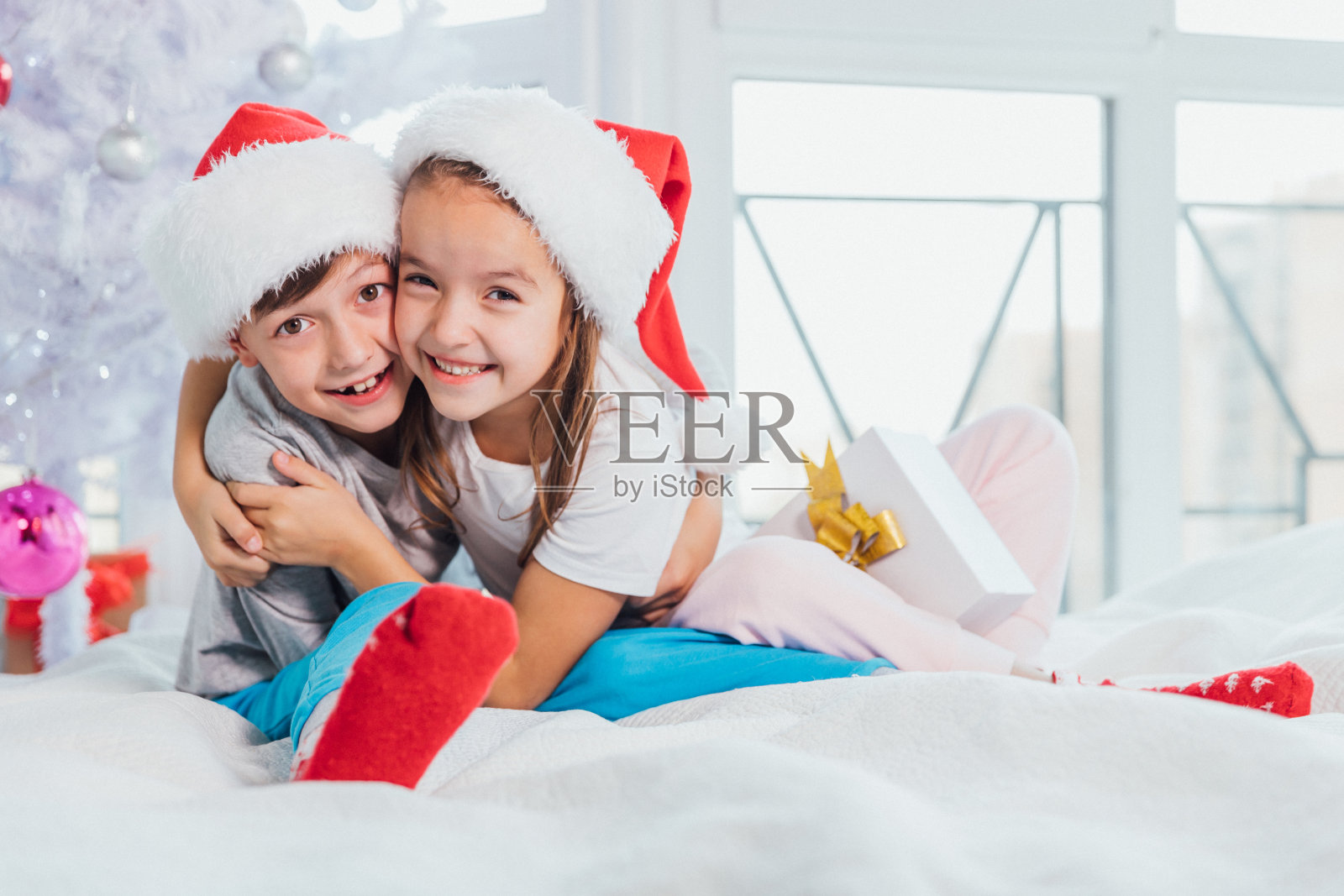 两个年轻的快乐可爱的欢笑的孩子，男孩和女孩，哥哥和妹妹在圣诞树附近玩耍的早晨。照片摄影图片