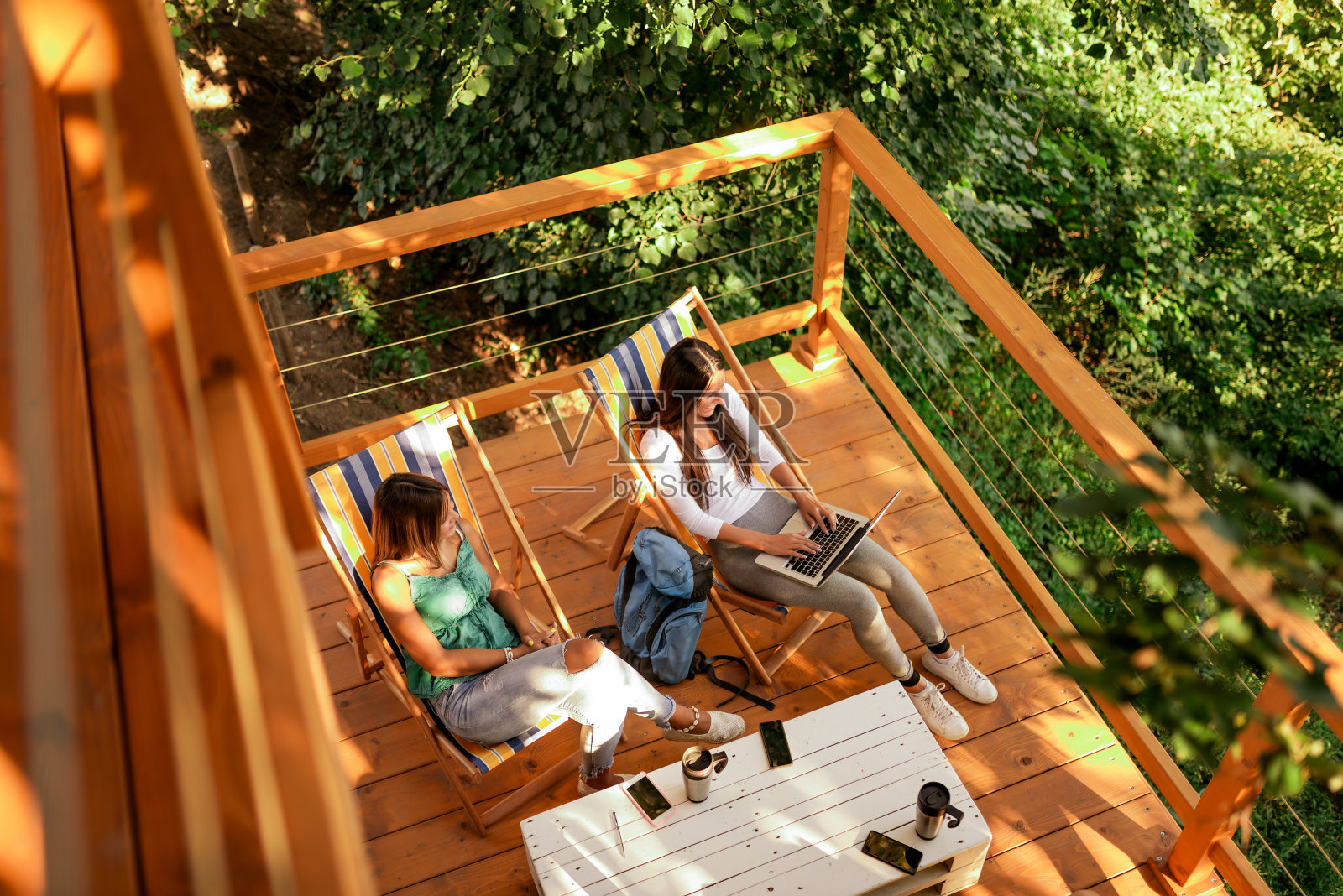 高角度的图像，两个年轻的女人享受在森林的木屋露台上。照片摄影图片