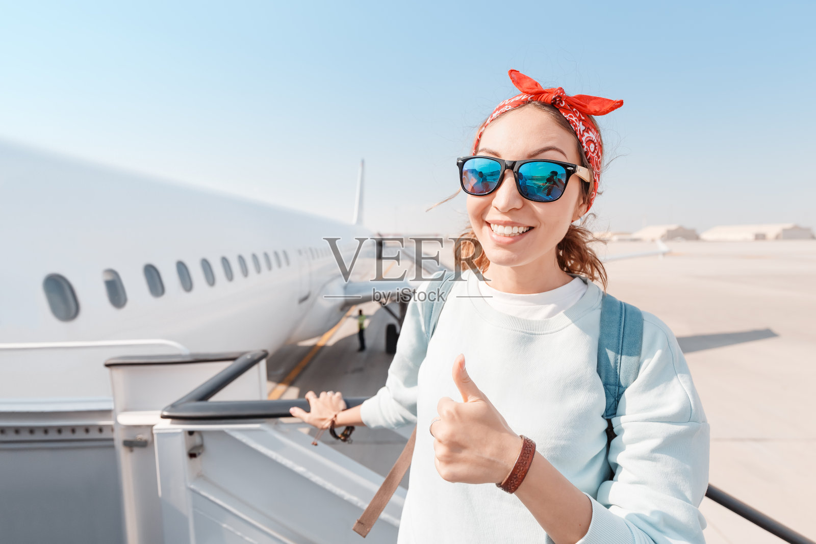 一个年轻的女孩在机场登上一架白色的大飞机时微笑着竖起大拇指。旅行的概念和战胜高空恐惧症照片摄影图片