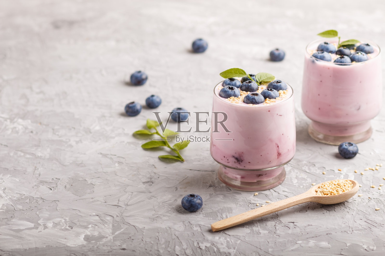 在灰色的混凝土背景下，用玻璃杯和木勺盛有蓝莓和芝麻的酸奶。侧视图，拷贝空间，选择性焦点。照片摄影图片