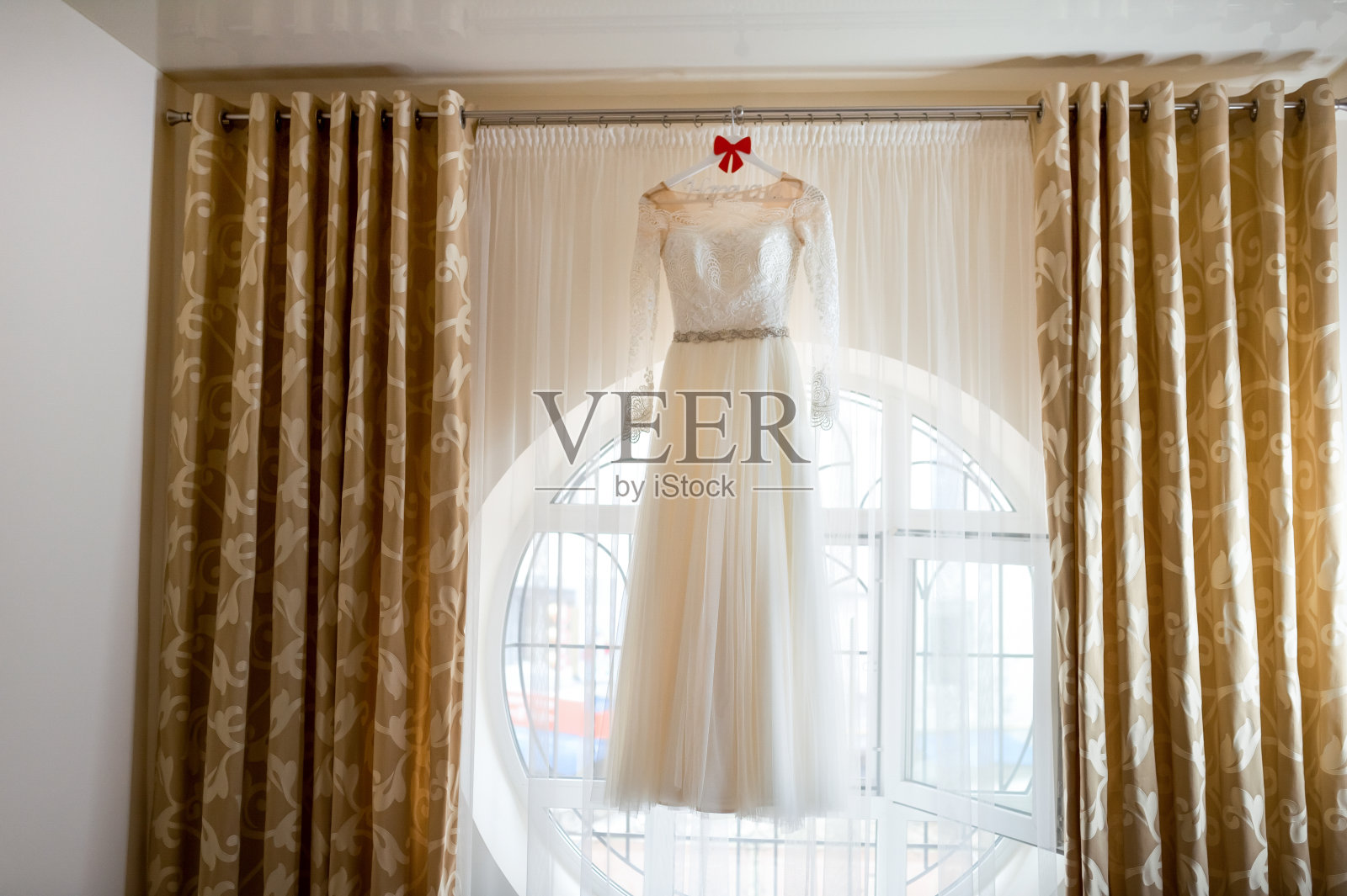 长长的漂亮的丝绸婚纱挂在窗户旁边。照片摄影图片