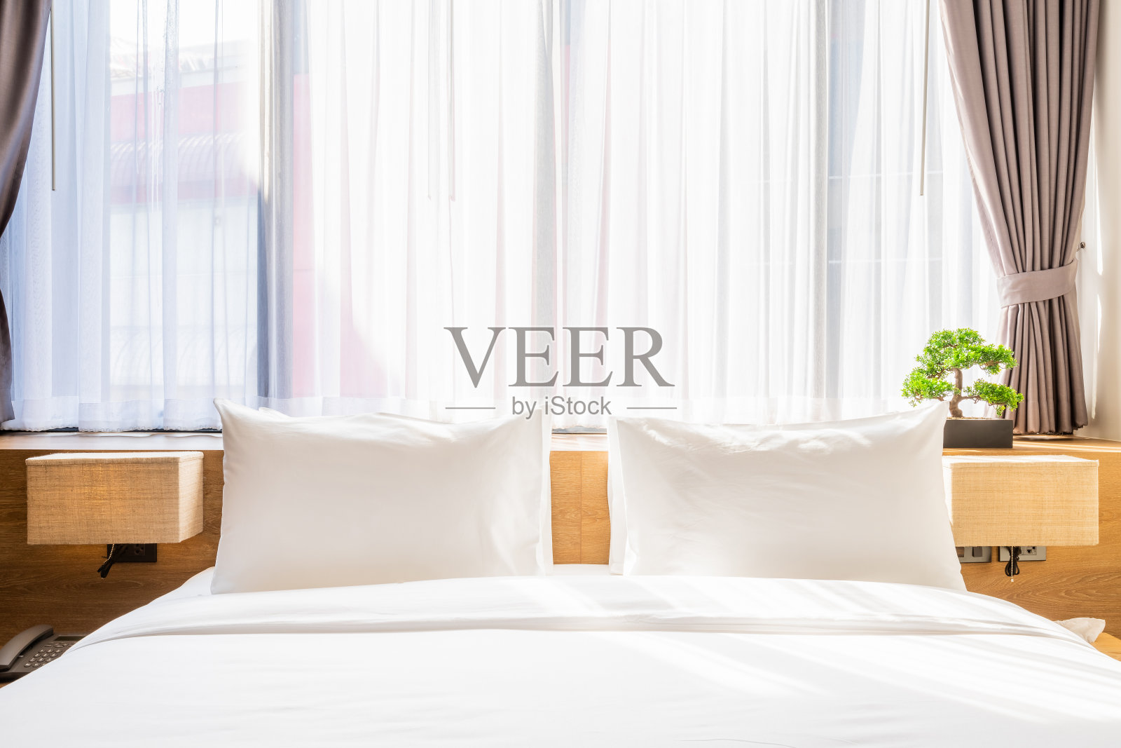 特写的白色枕头在床上装饰灯和绿树在花盆在酒店卧室内部。照片摄影图片