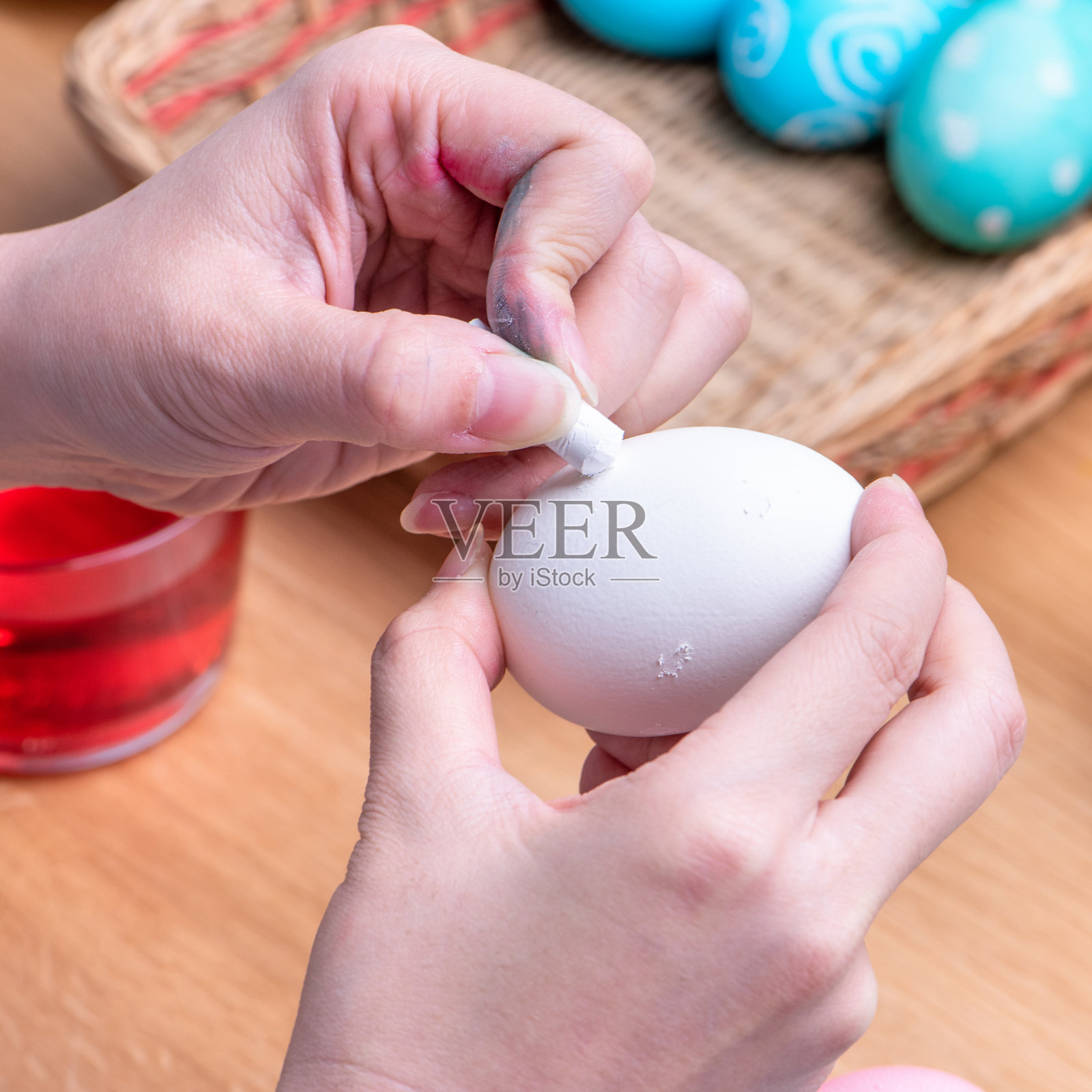 复活节彩蛋的准备-年轻的妇女正在用蜡笔画白色的鸡蛋，然后在家里厨房的桌子上染色。照片摄影图片