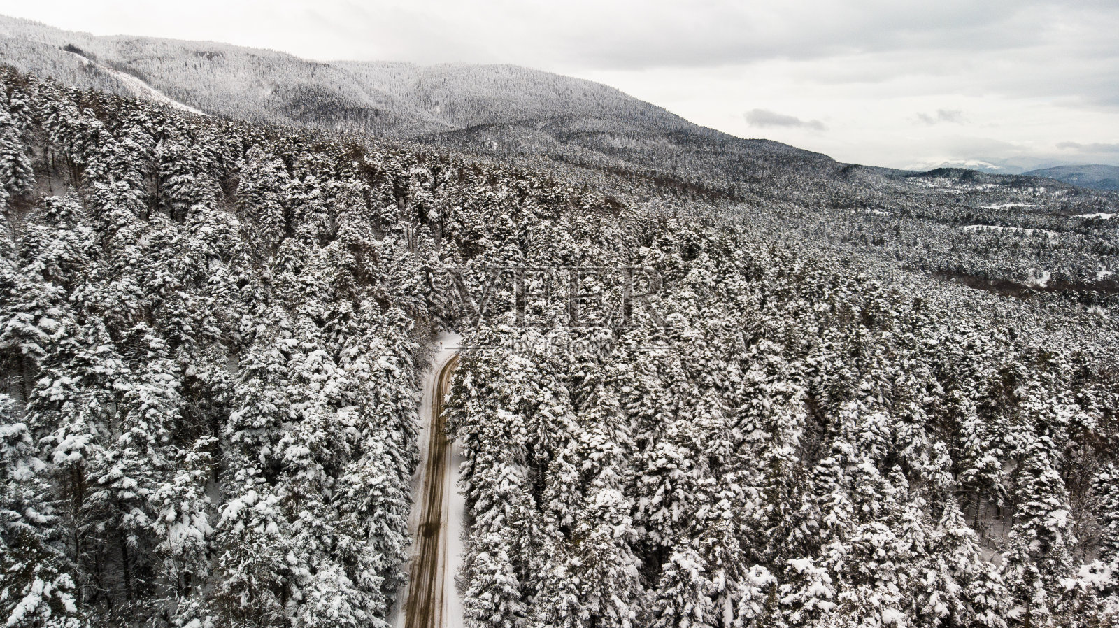 多风的道路在积雪覆盖的森林，从上到下鸟瞰图照片摄影图片