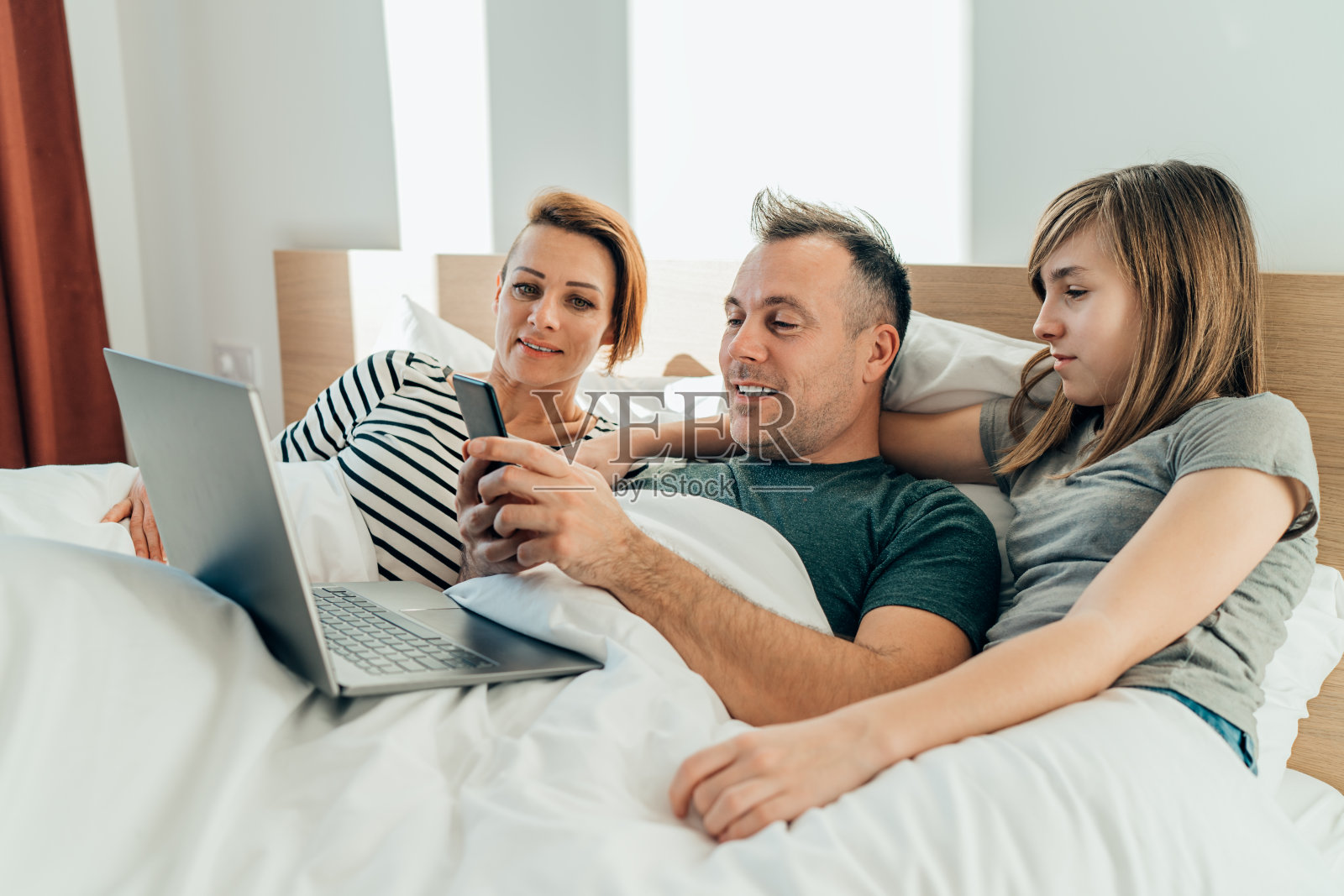 家人躺在床上玩智能手机照片摄影图片