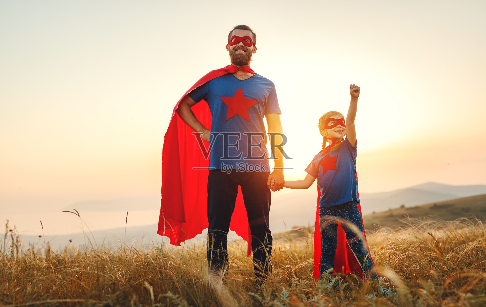父亲节的概念。爸爸和女儿穿着英雄超级英雄的服装在日落照片摄影图片