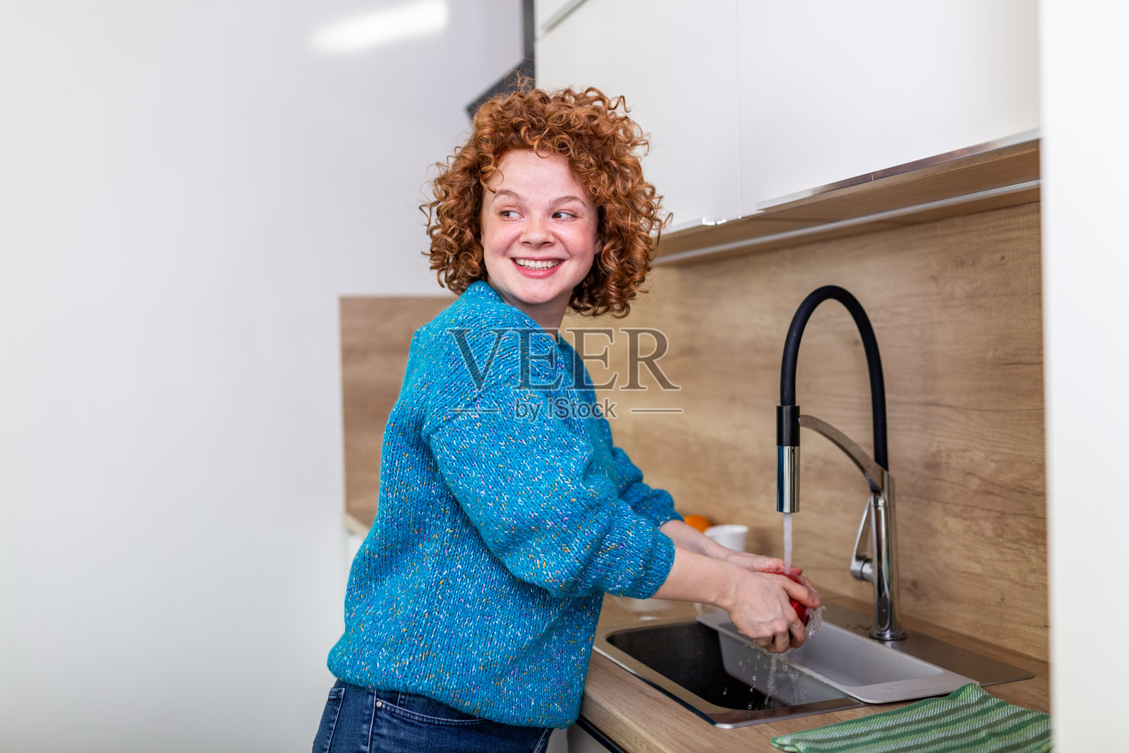 可爱的红卷发女孩在厨房水槽里洗苹果。年轻女子在水龙头下用水清洗她的水果。每天摄入维生素与水果，饮食和健康饮食照片摄影图片