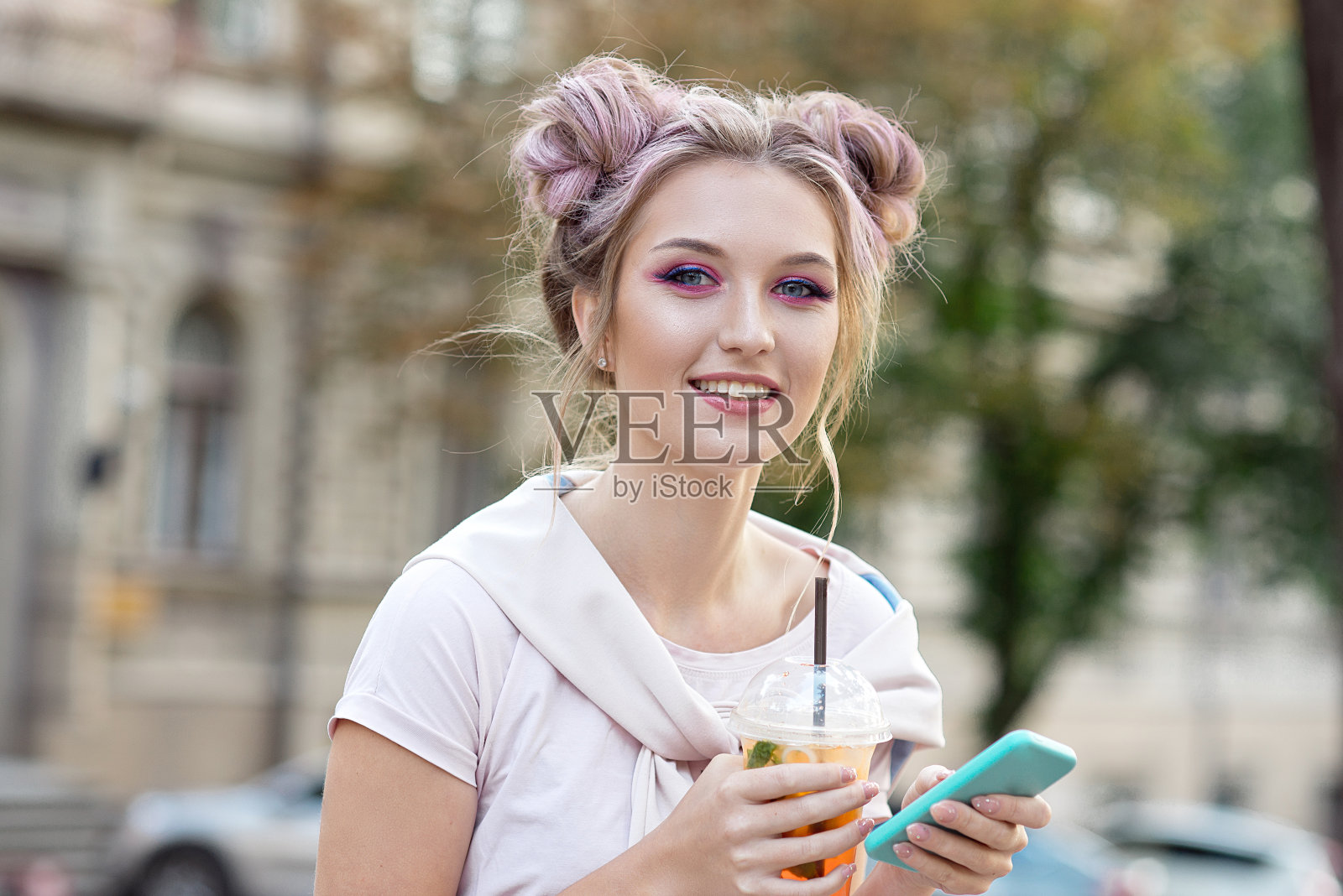 年轻漂亮的女孩在户外散步后用塑料外卖杯喝新鲜的果汁。健康的生活方式。苗条的金发，粉红色的头发照片摄影图片