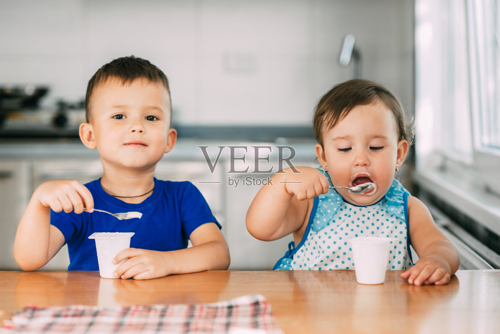 一个温暖的夏日，男孩和女孩在厨房里吃酸奶照片摄影图片
