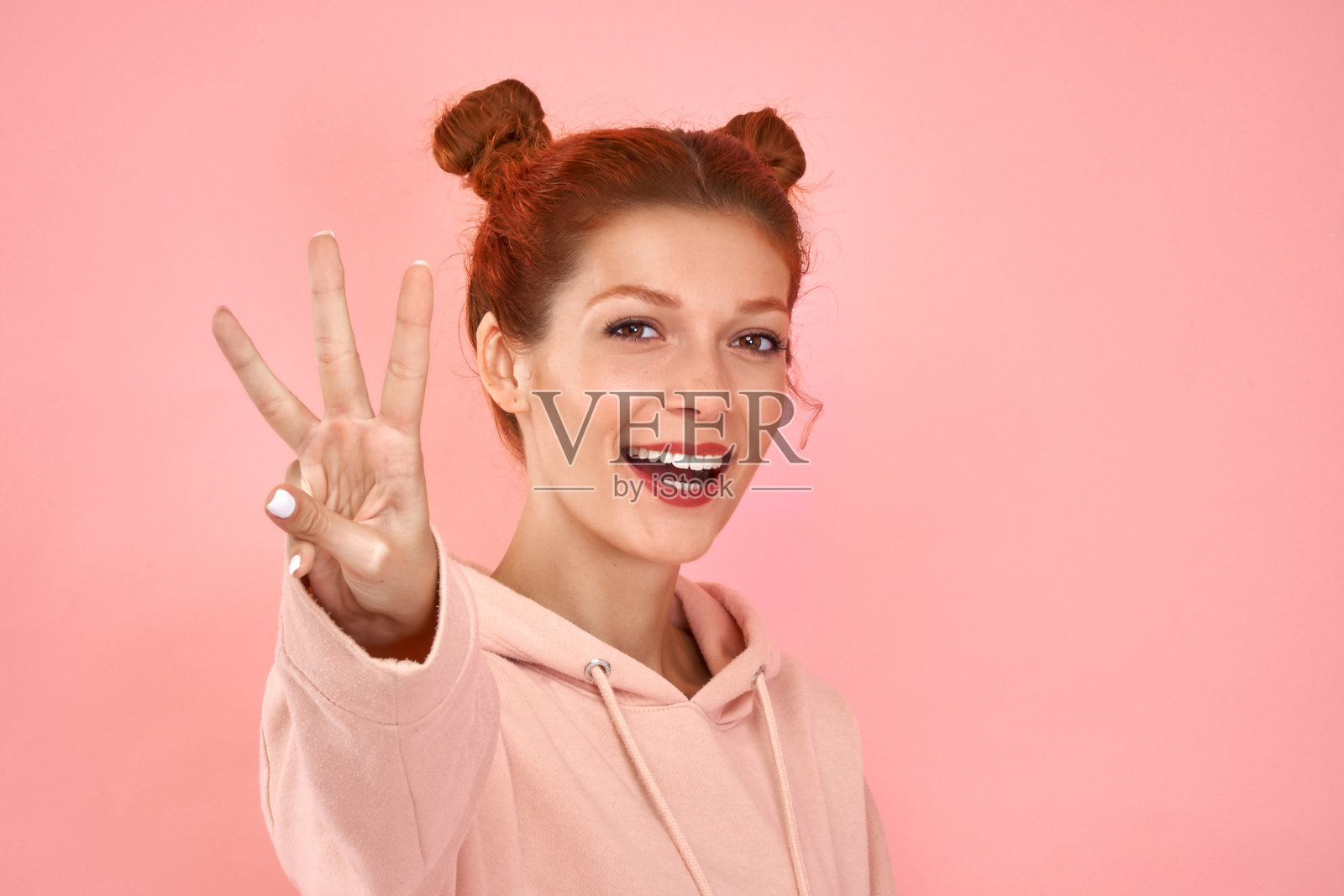照片波浪卷迷人的白种人年轻红发女人微笑牙齿向你展示三个手指孤立在粉红色的工作室背景。计算姿态。肢体语言和非语言交流照片摄影图片