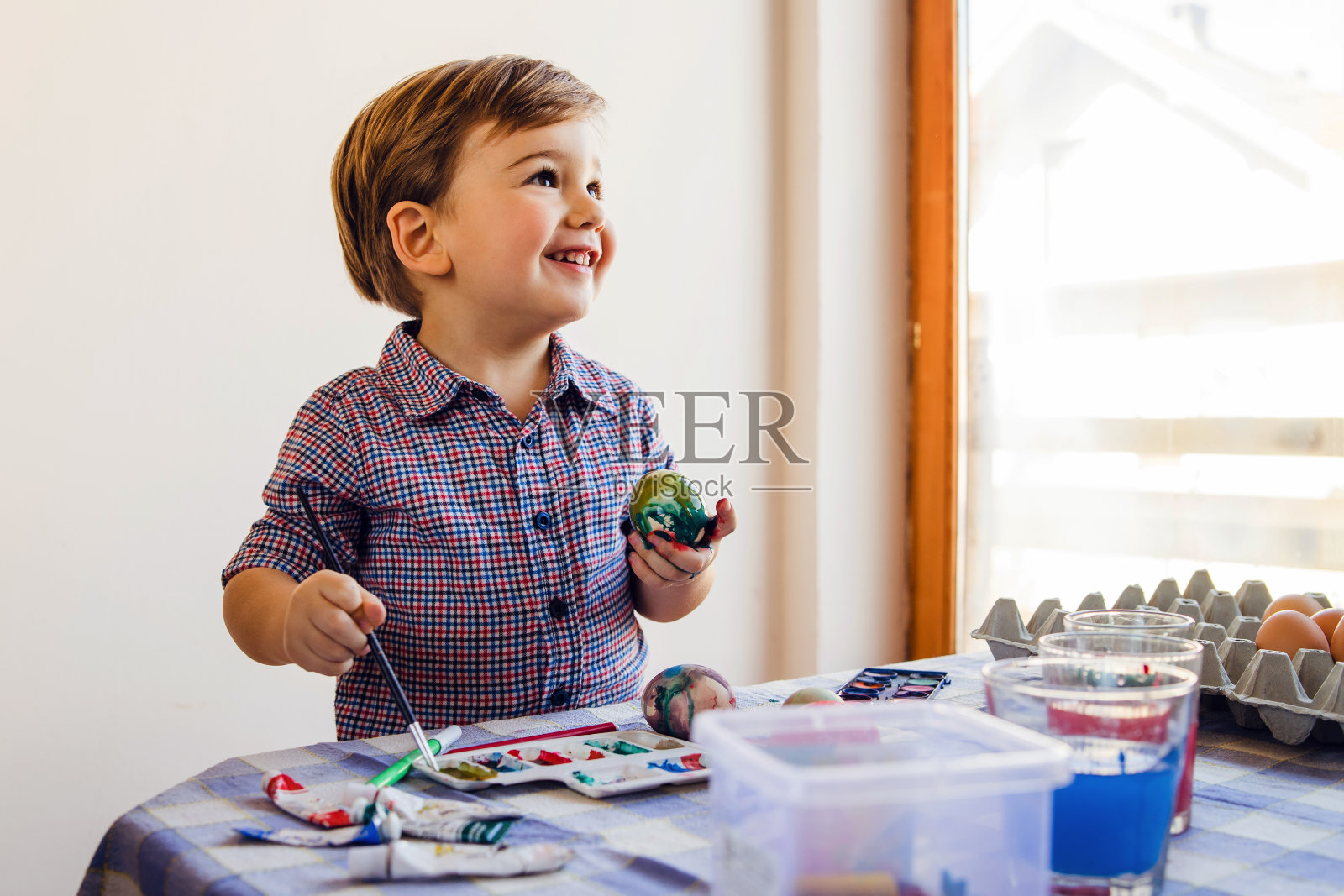 白种人小男孩两岁，拿着用水彩笔画的复活节彩蛋，站在家里的桌子旁为节日装饰微笑照片摄影图片