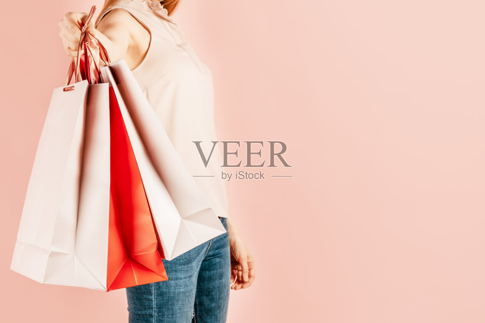 购物和消费。年轻漂亮的女孩拿着纸袋购物。粉红色的背景。挑选节日礼物。为自己购物。模拟了照片摄影图片