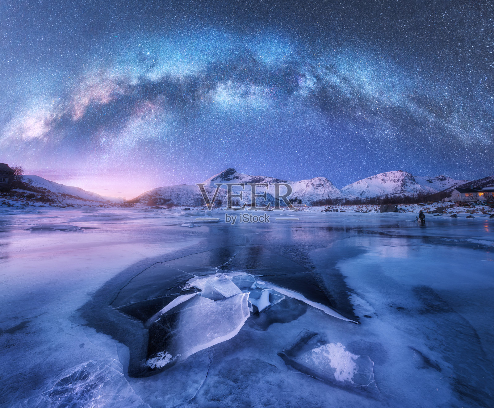 冬日夜晚，挪威罗浮敦群岛冰雪覆盖的山脉和海岸上空的银河。北极景观有蓝色的星空、水、冰、雪石、银河。空间和星系照片摄影图片