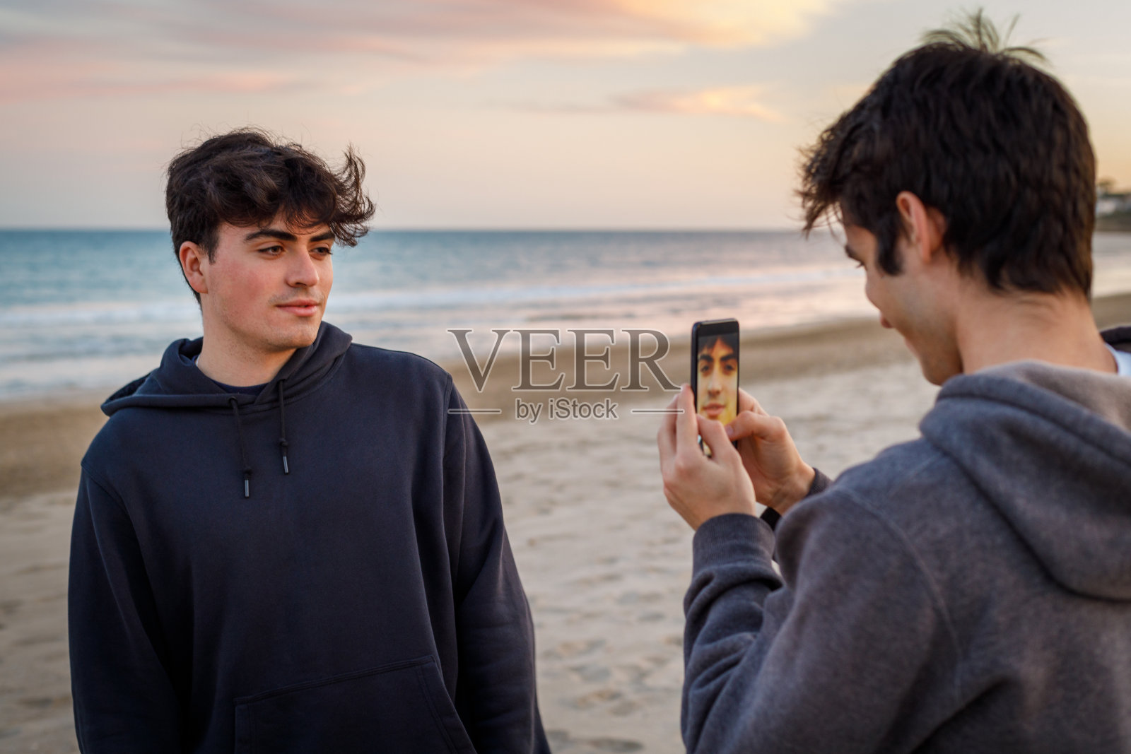 一个大学生在海滩上用手机给朋友拍日落的照片照片摄影图片