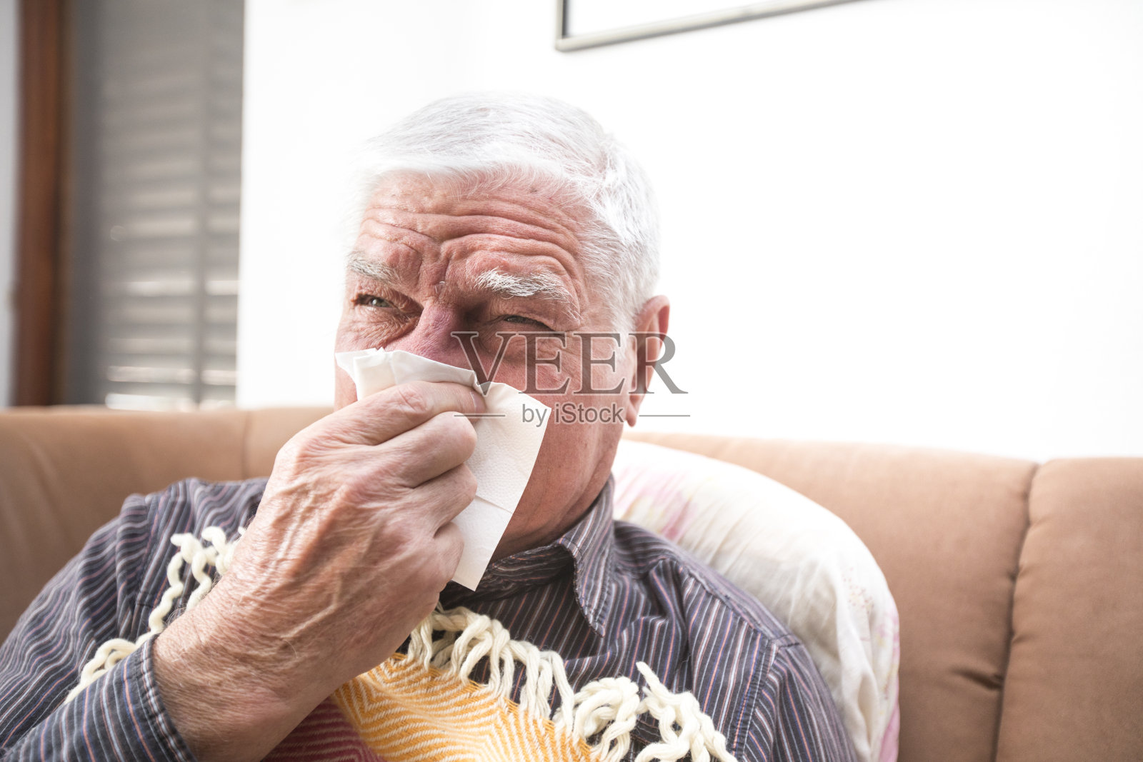 年长的成年人一边擤鼻涕一边坐在沙发上照片摄影图片
