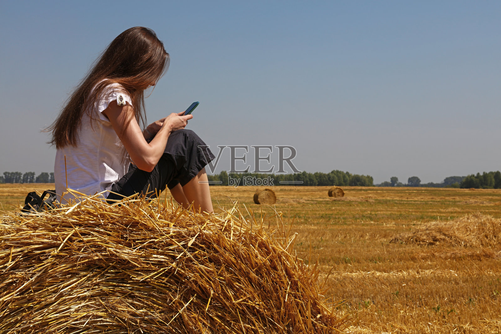 年轻女子坐在田里的稻草捆上照片摄影图片