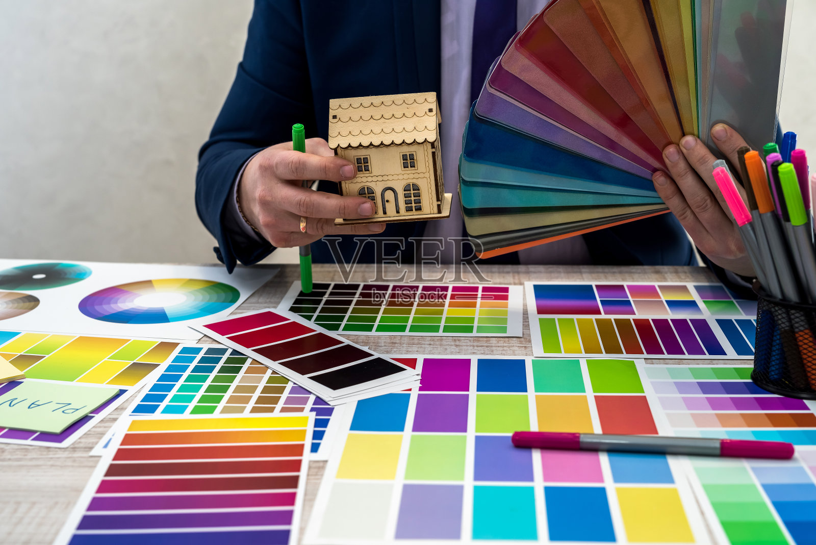 图形或室内年轻设计师在西装选择颜色从样本或目录调色板指南在工作场所。平面设计师与油漆调色板样品在桌子上照片摄影图片