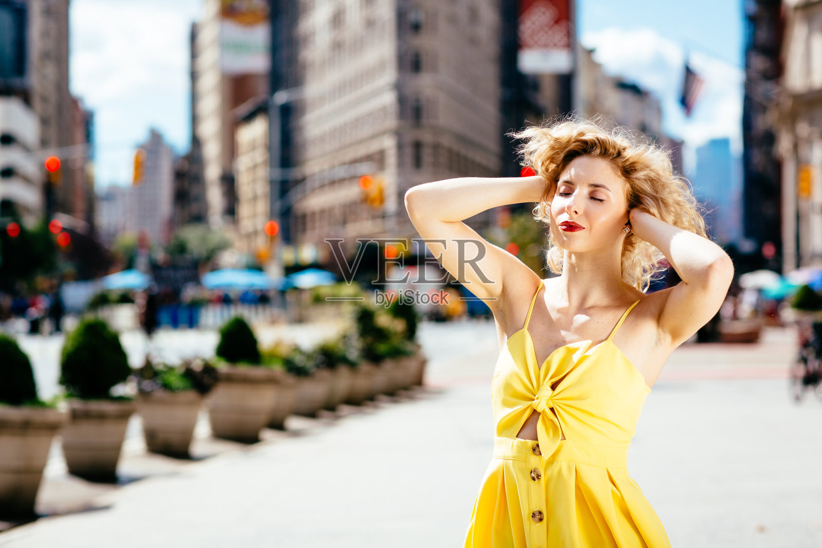 在纽约熨斗大厦前，一名身穿黄色连衣裙、双手放在脑后的妇女照片摄影图片