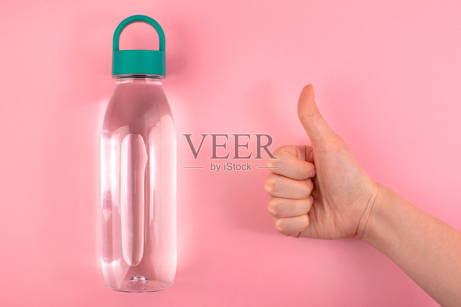 粉色背景的可重复使用的水瓶和女性竖起的大拇指。最小的健康的生活方式。照片摄影图片