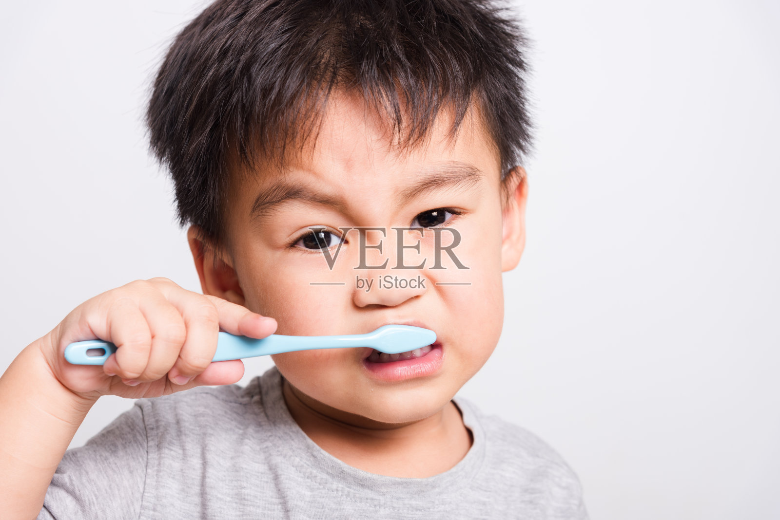 特写亚洲人的脸，小男孩手里拿着牙刷他自己在白色的背景上刷牙照片摄影图片