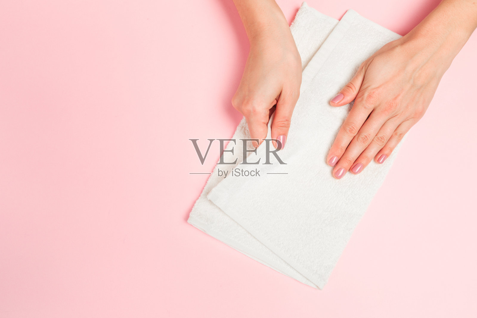 美丽的年轻女人的手与白色护理毛巾在柔和的粉红色背景-图像照片摄影图片