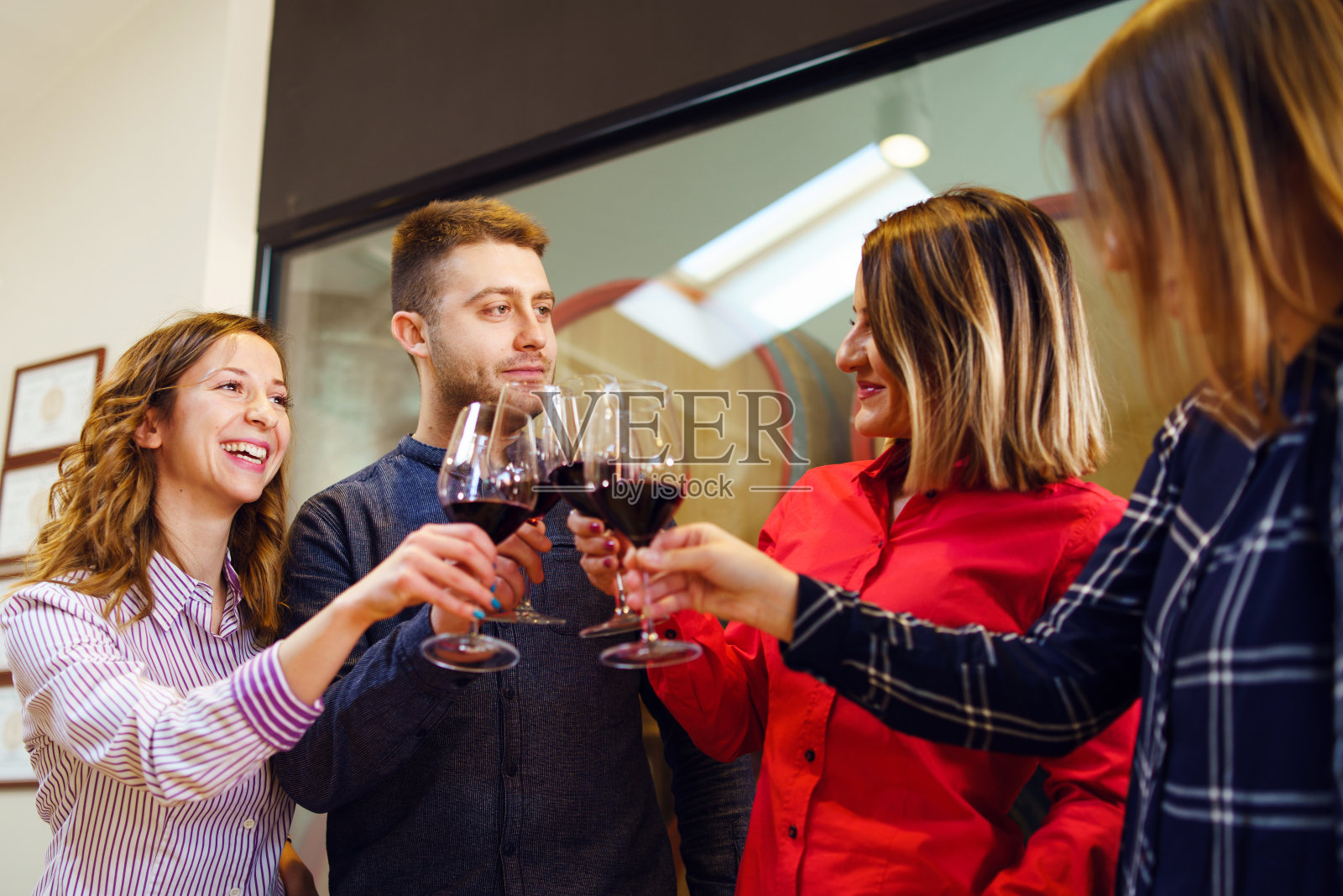 一群白人朋友或家人站在酿酒厂或餐馆的桌子旁，拿着一杯红酒向一名年轻男子和三名身穿衬衫微笑的女子敬酒照片摄影图片