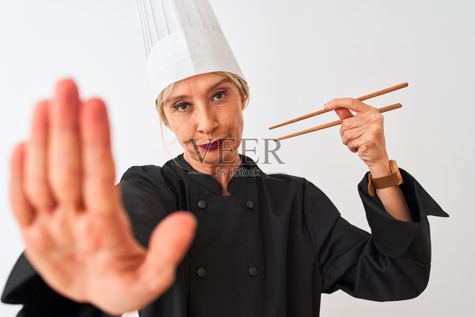 中年厨师妇女戴着帽子，拿着筷子，在孤立的白色背景下，张开手做着停止标志，严肃而自信的表情，防御手势照片摄影图片