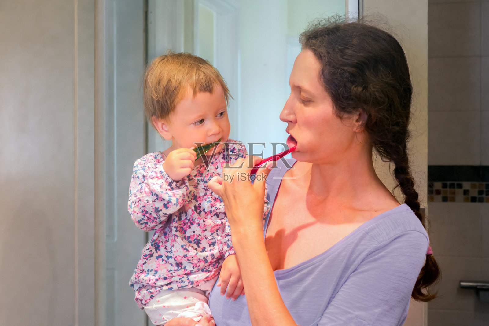 宝宝在妈妈的手上和妈妈一起刷牙。母女俩在浴室里刷牙。第一次牙齿。牙科的概念。妈妈在给孩子刷牙。照片摄影图片