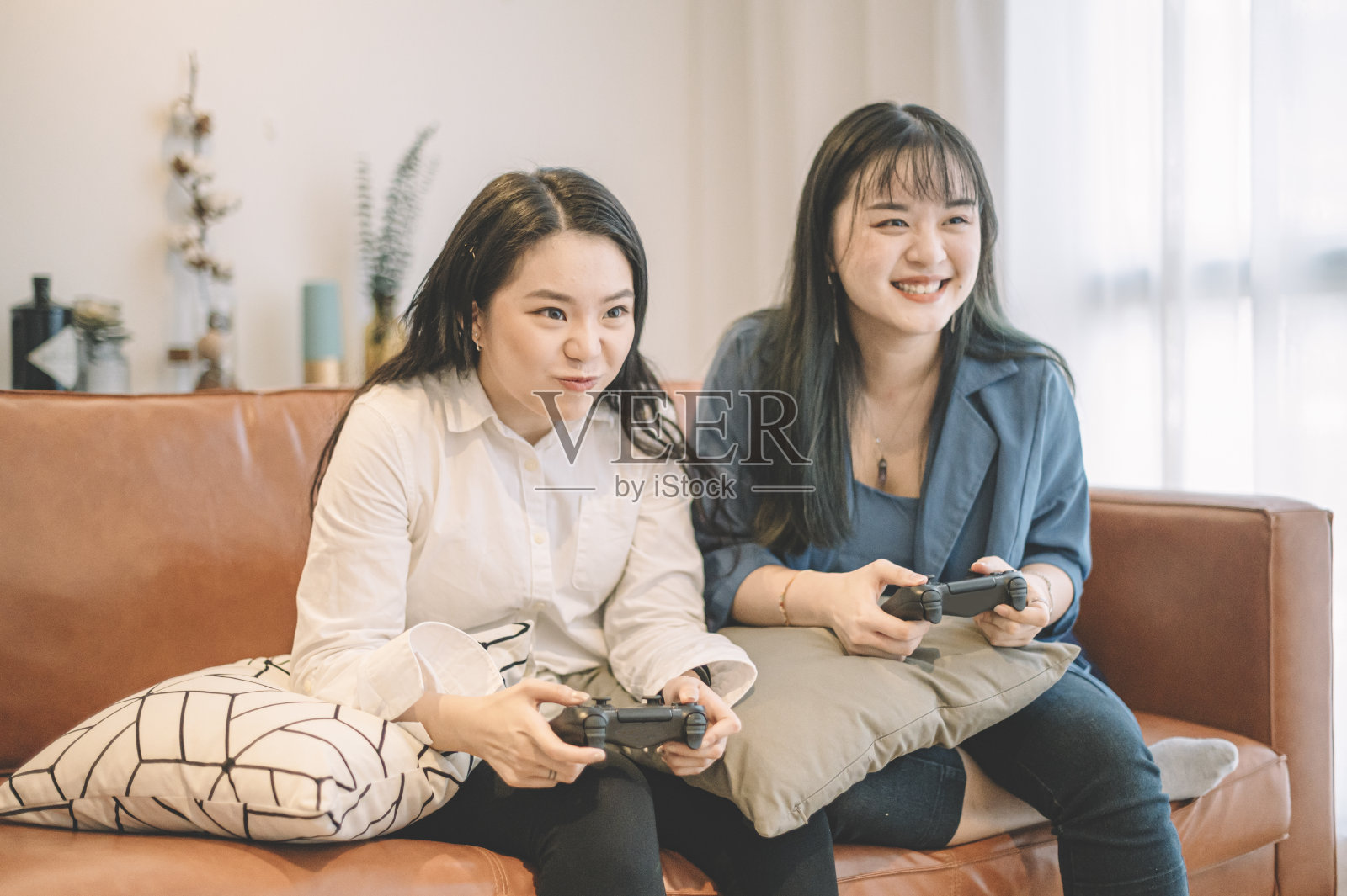 两个亚洲华人女性朋友坐在沙发上玩电子游戏照片摄影图片