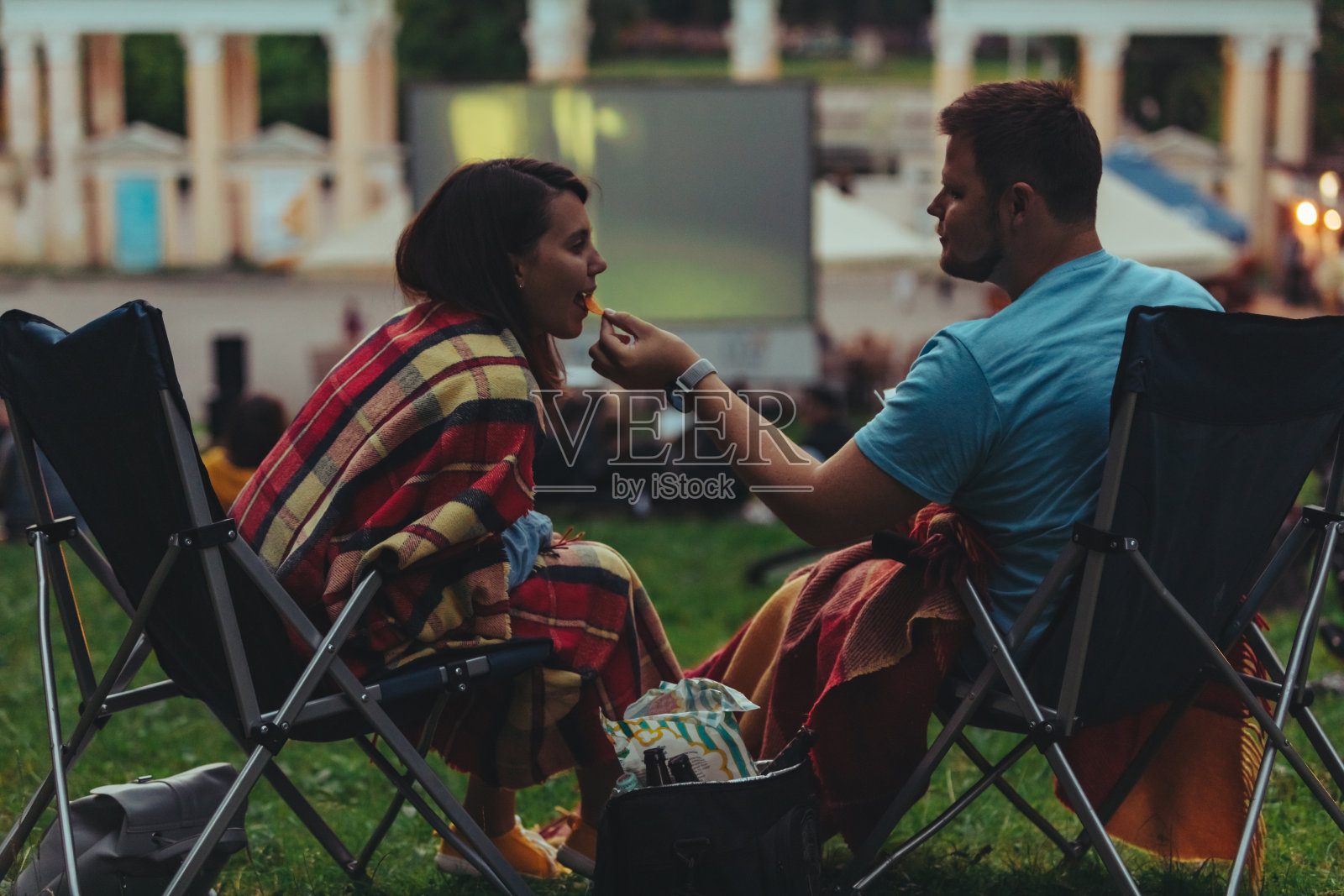 一对夫妇坐在城市公园的露营椅上在露天电影院看电影照片摄影图片