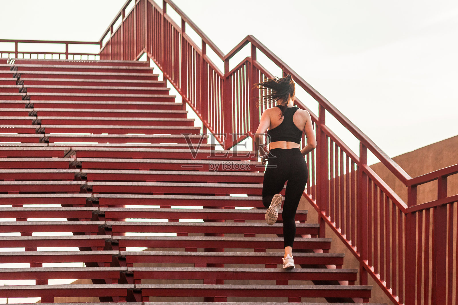 后视图的跑步运动员，合身的黑发女孩在黑色运动服，紧身裤和上衣，跑上楼照片摄影图片