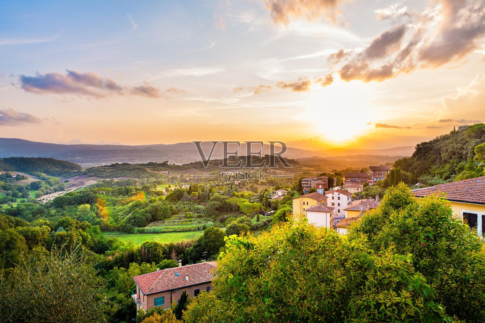 在意大利托斯卡纳的Chiusi小镇上，色彩斑斓的傍晚日落，在山野上的房屋屋顶，连绵起伏的丘陵景观和阳光下如画的城市景观照片摄影图片