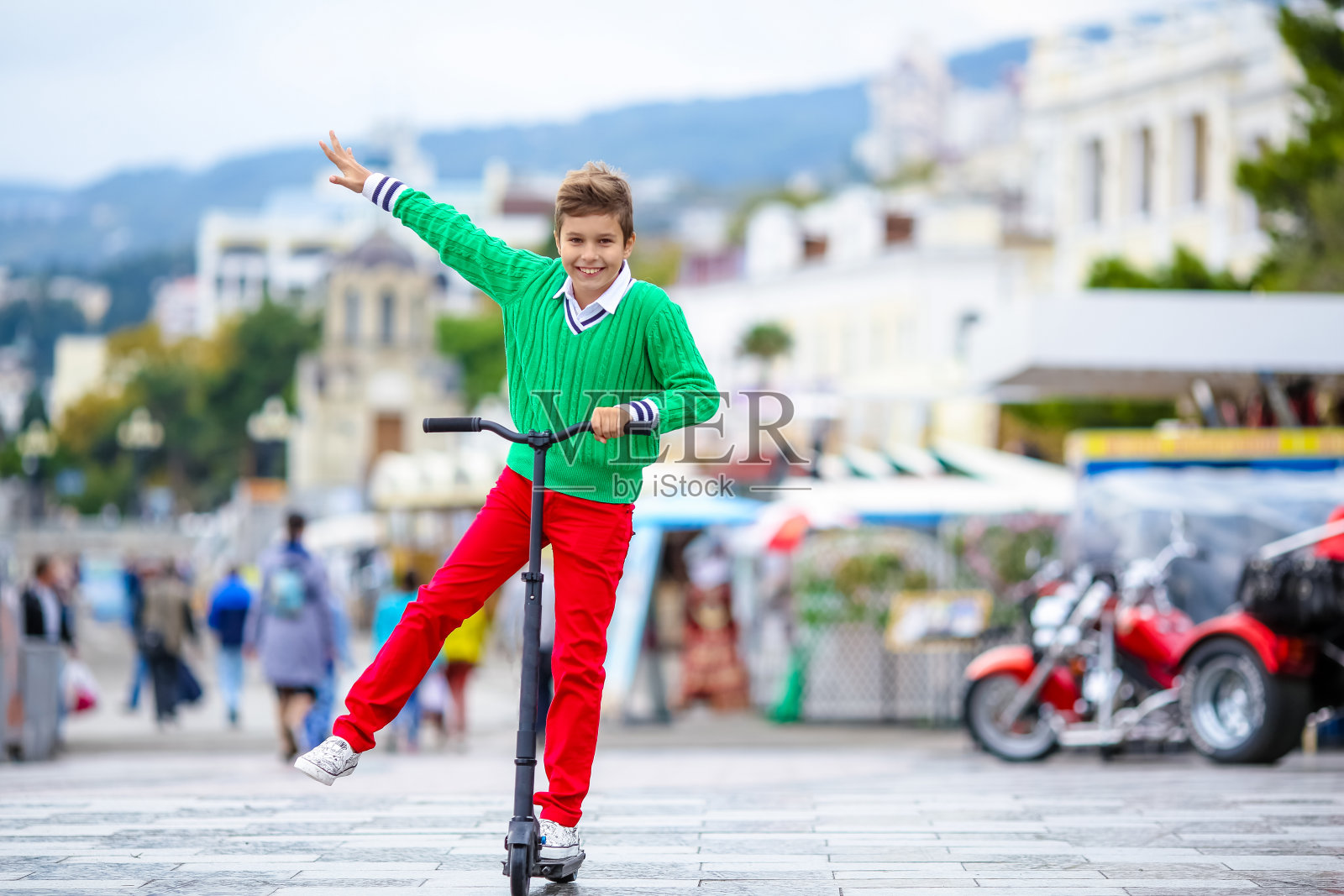 一个穿着鲜红色裤子的男孩在开阔的地方骑着滑板车照片摄影图片