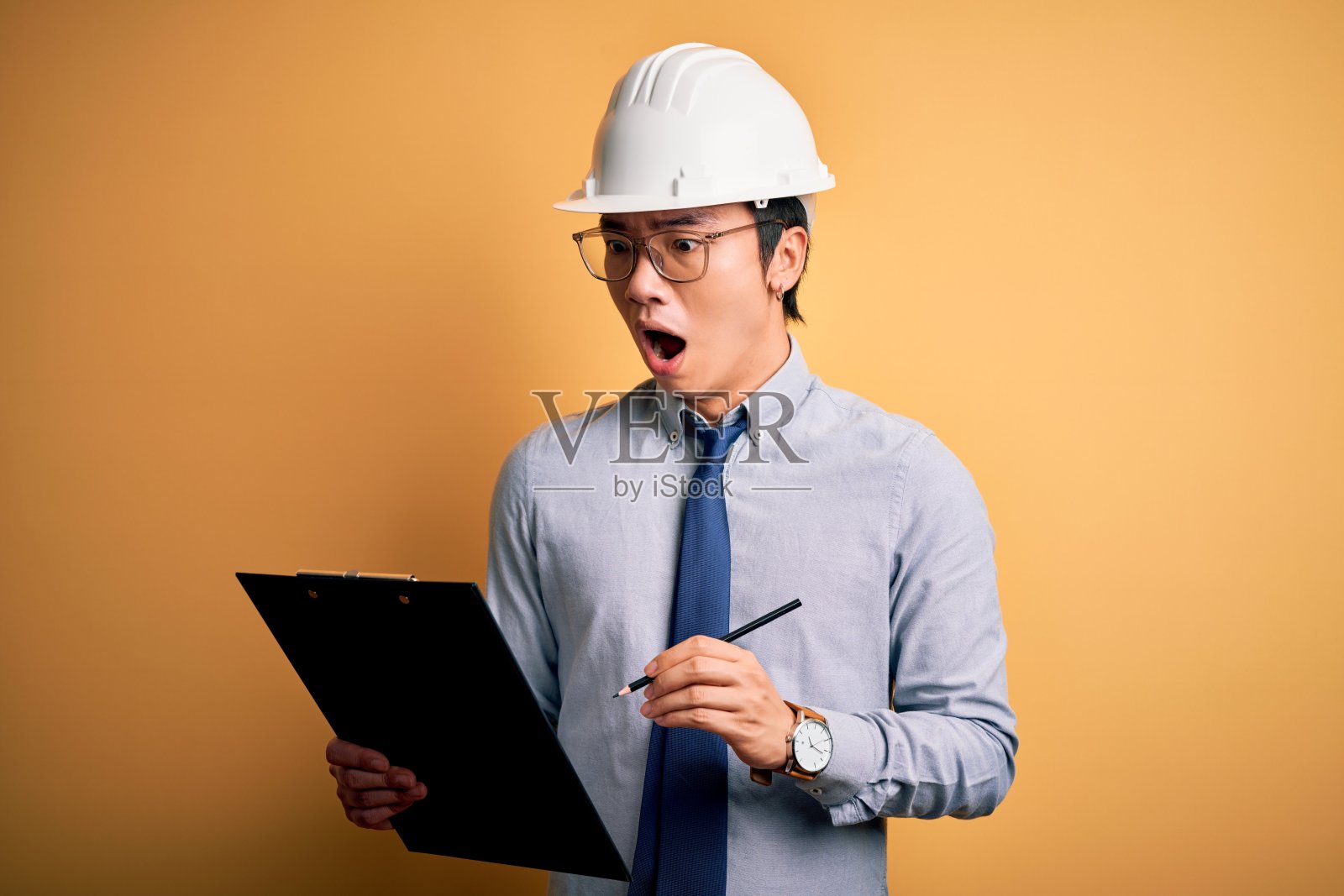 年轻英俊的中国工程师男子戴着安全帽，手里拿着剪贴板吓得一脸惊讶，害怕又兴奋，带着恐惧的表情照片摄影图片