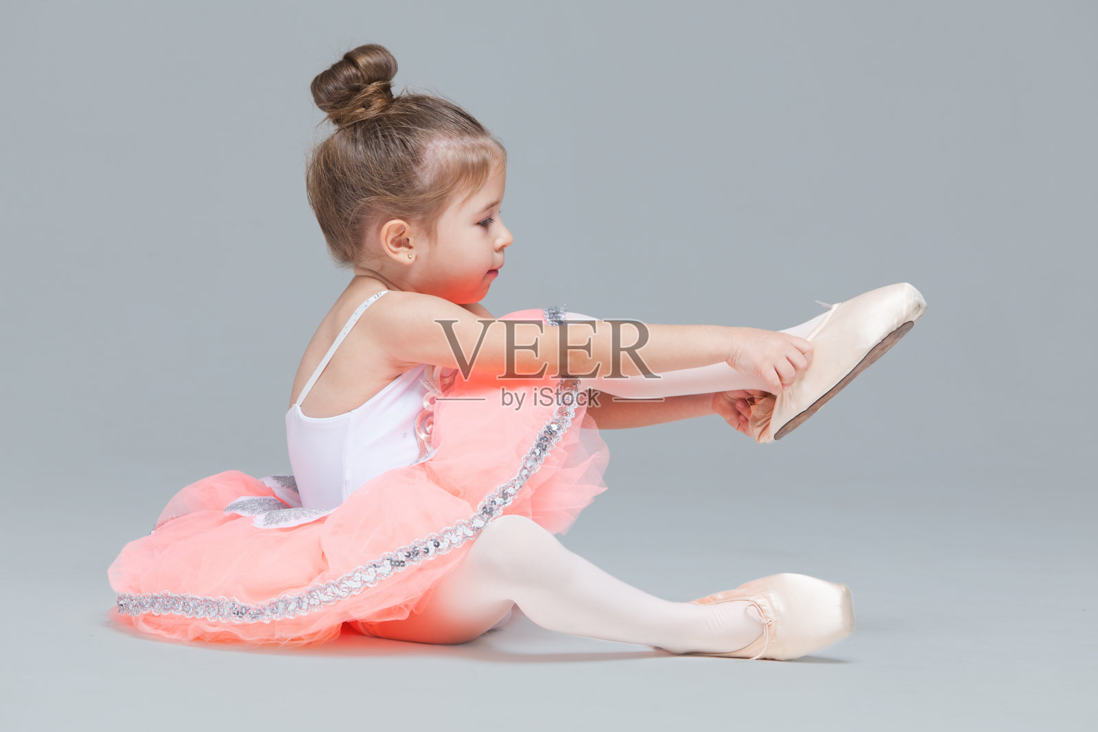 可爱迷人的芭蕾舞小女孩穿着粉红色的芭蕾舞裙坐在地板上试着穿上芭蕾舞鞋照片摄影图片