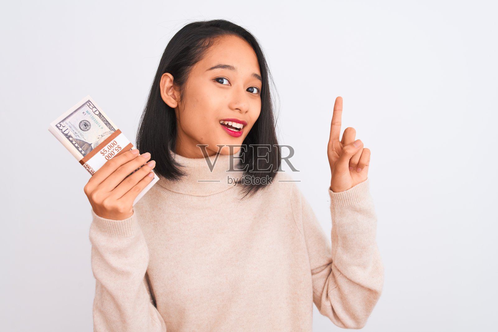 年轻美丽的中国女人拿着美元站在孤立的白人背景惊讶地提出一个想法或问题，用幸福的脸指着手指，第一照片摄影图片