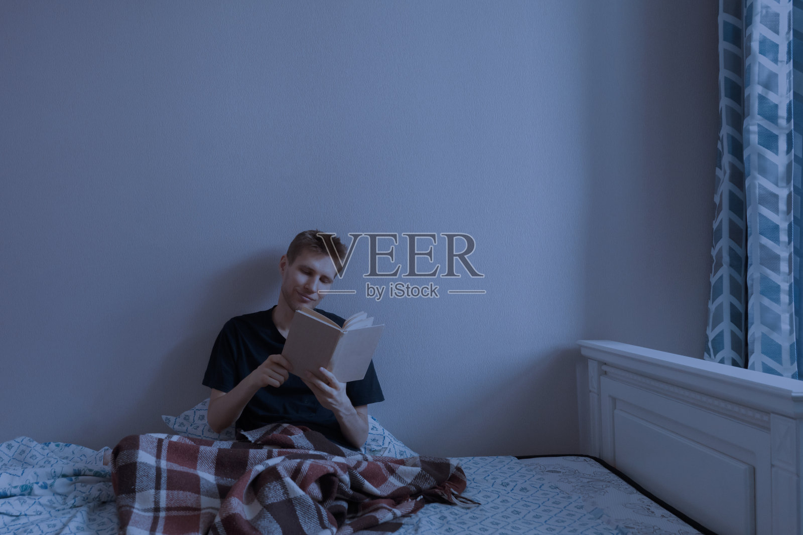 年轻男子晚上睡觉前躺在家里卧室的床上看书照片摄影图片