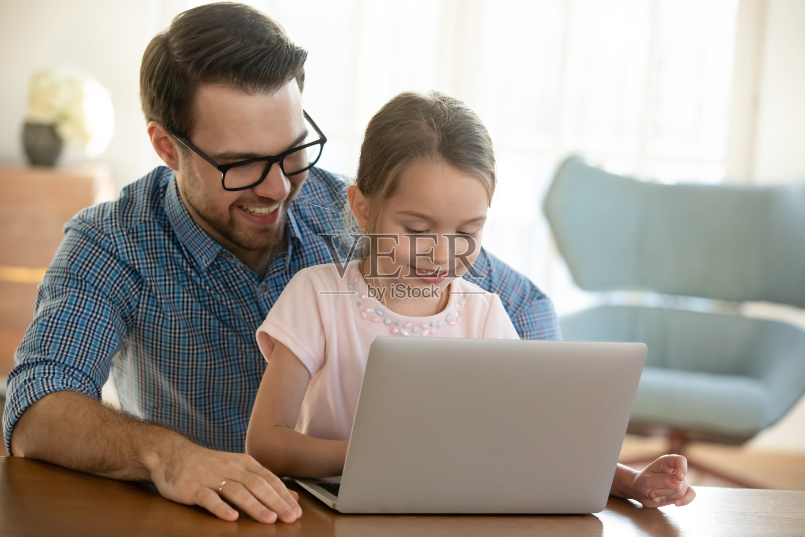 年轻的父亲用电脑抱着学龄前的小女儿。照片摄影图片