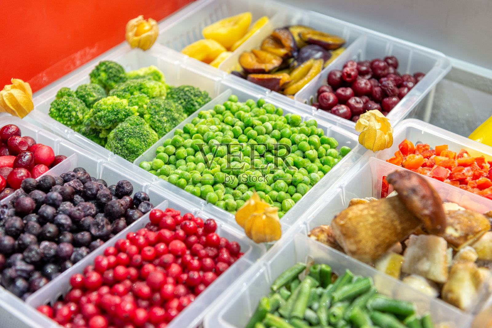 冷冻水果和蔬菜。浆果，蘑菇，豆类等等。产品被倒入塑料盒中。在框架的中心是绿色的豌豆照片摄影图片