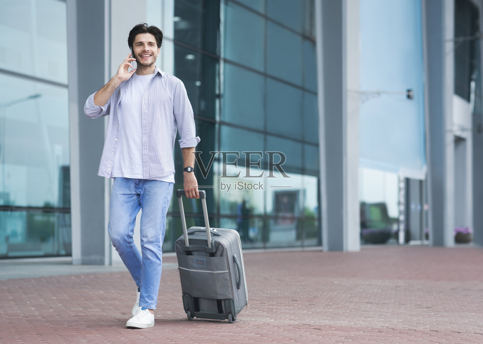 一名男子提着行李箱走在机场外，用手机打电话照片摄影图片