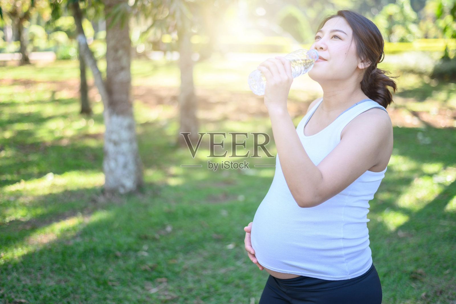 年轻的亚洲孕妇在公园放松和锻炼后饮用干净的水的肖像。照片摄影图片
