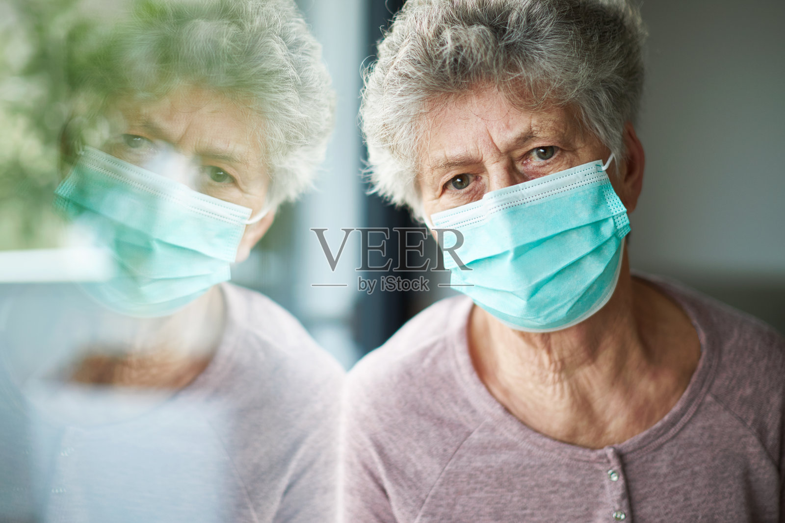 一位老妇人或老奶奶戴着呼吸器或医用口罩望着窗外照片摄影图片