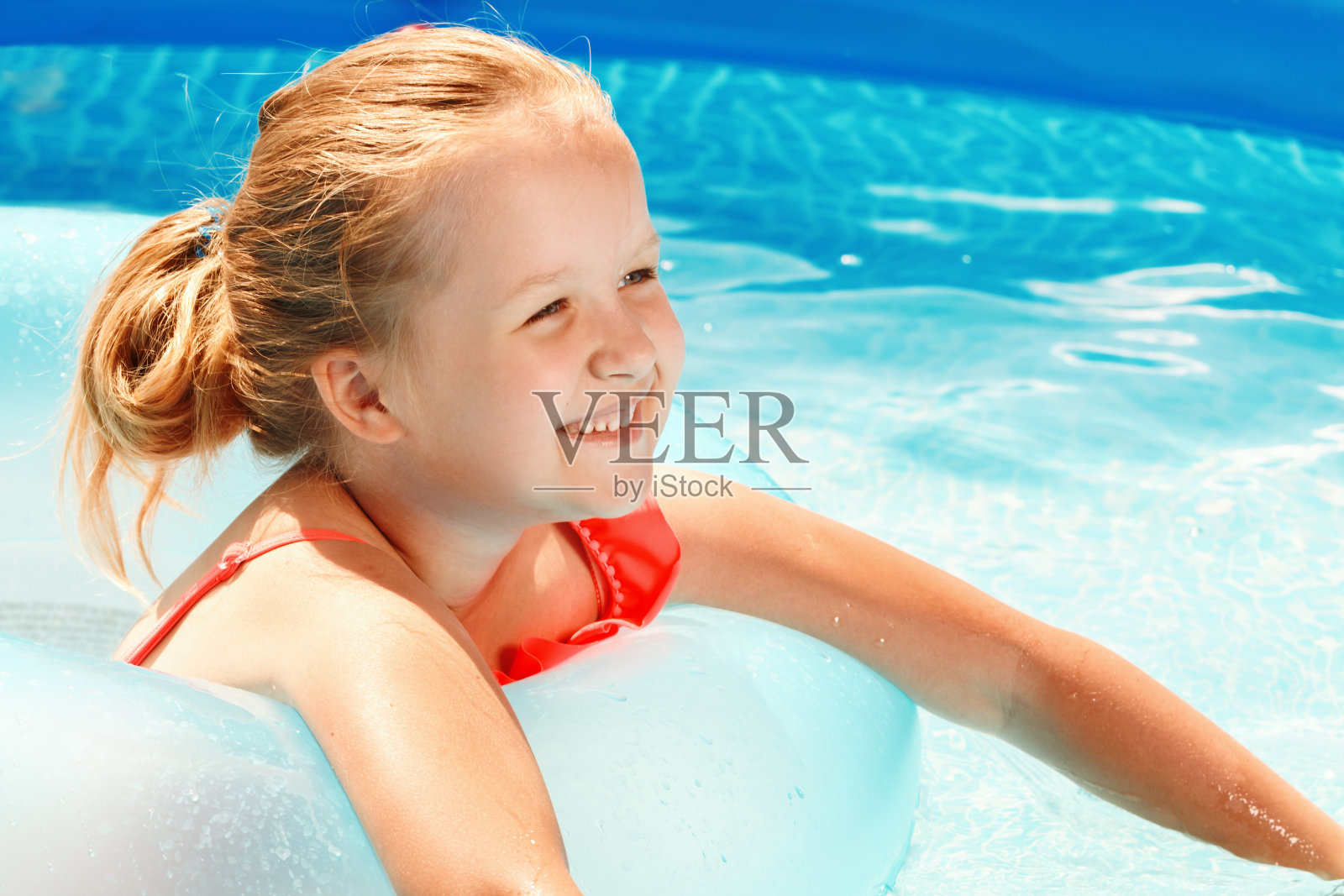 在一个阳光明媚的日子里，可爱的小女孩在游泳池的橡皮环上游泳。暑假里的孩子照片摄影图片