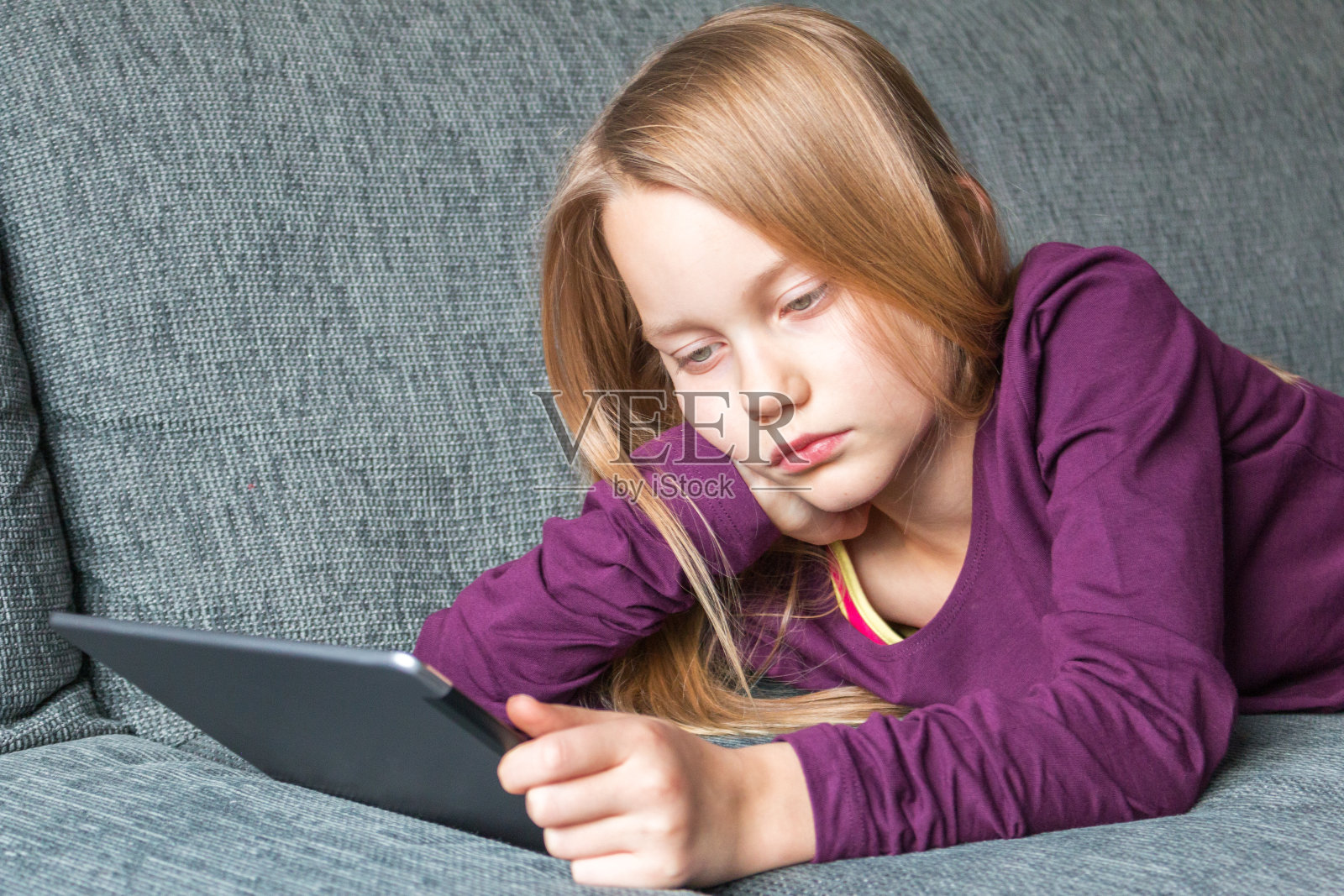 一个女孩躺在沙发上，手里拿着一台平板电脑照片摄影图片