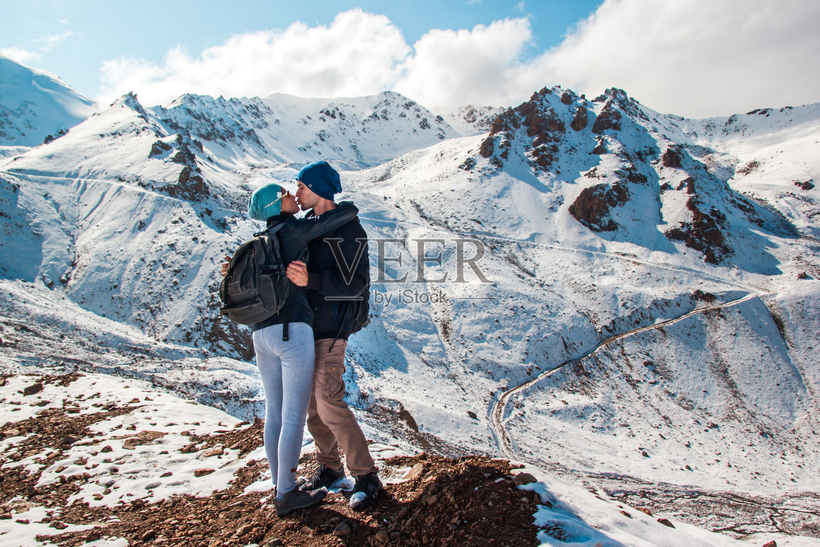 在雪山的背景下，一个男人亲吻一个女人的嘴唇。在山上度假。照片摄影图片