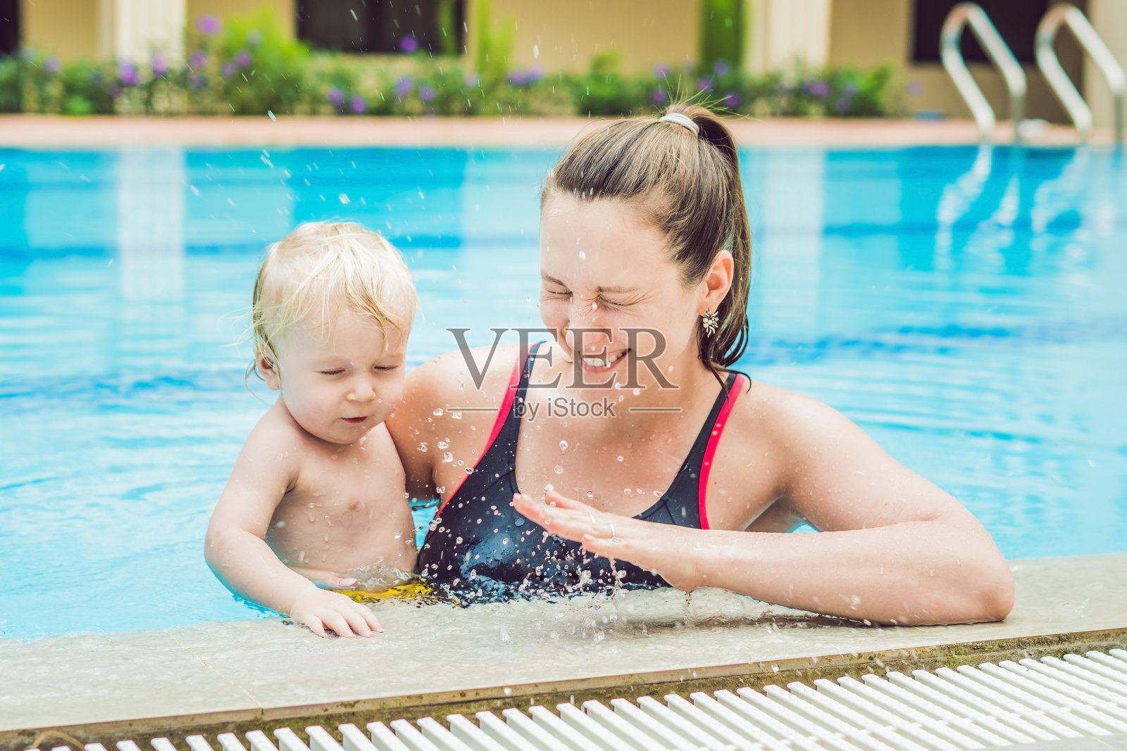 一位年轻的母亲教她的小儿子如何在游泳池里游泳照片摄影图片
