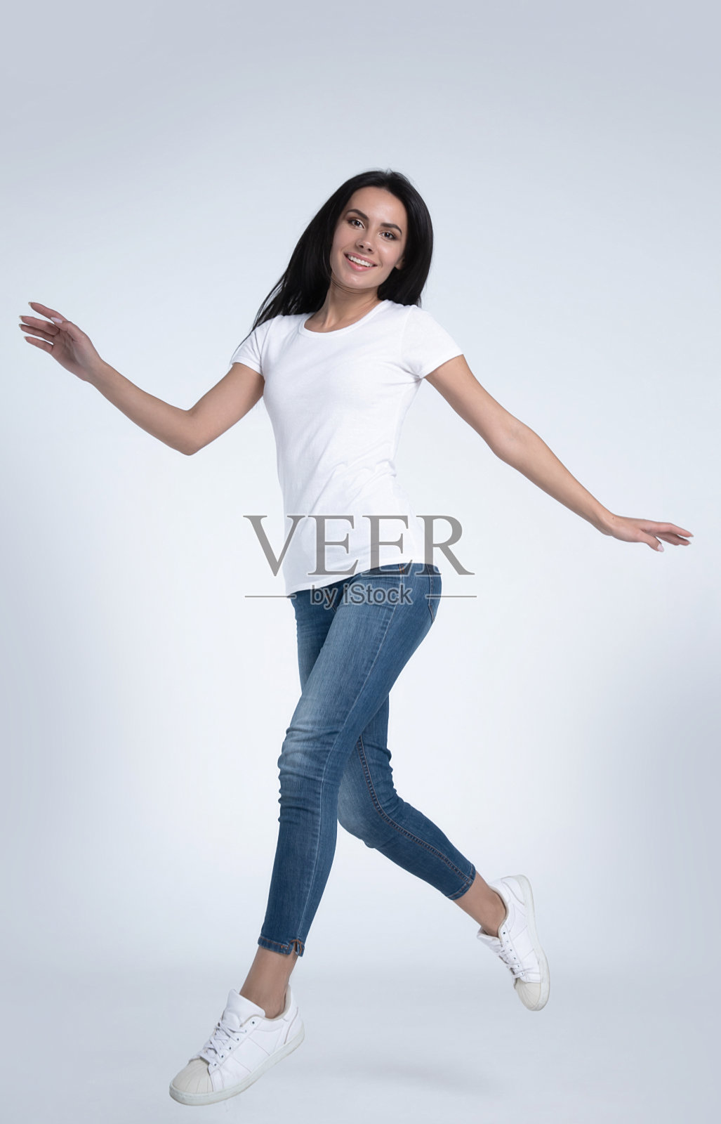 兴奋和快乐的美丽的女人是跳跃和呼喊在白色的t恤和牛仔裤孤立的背景。照片摄影图片